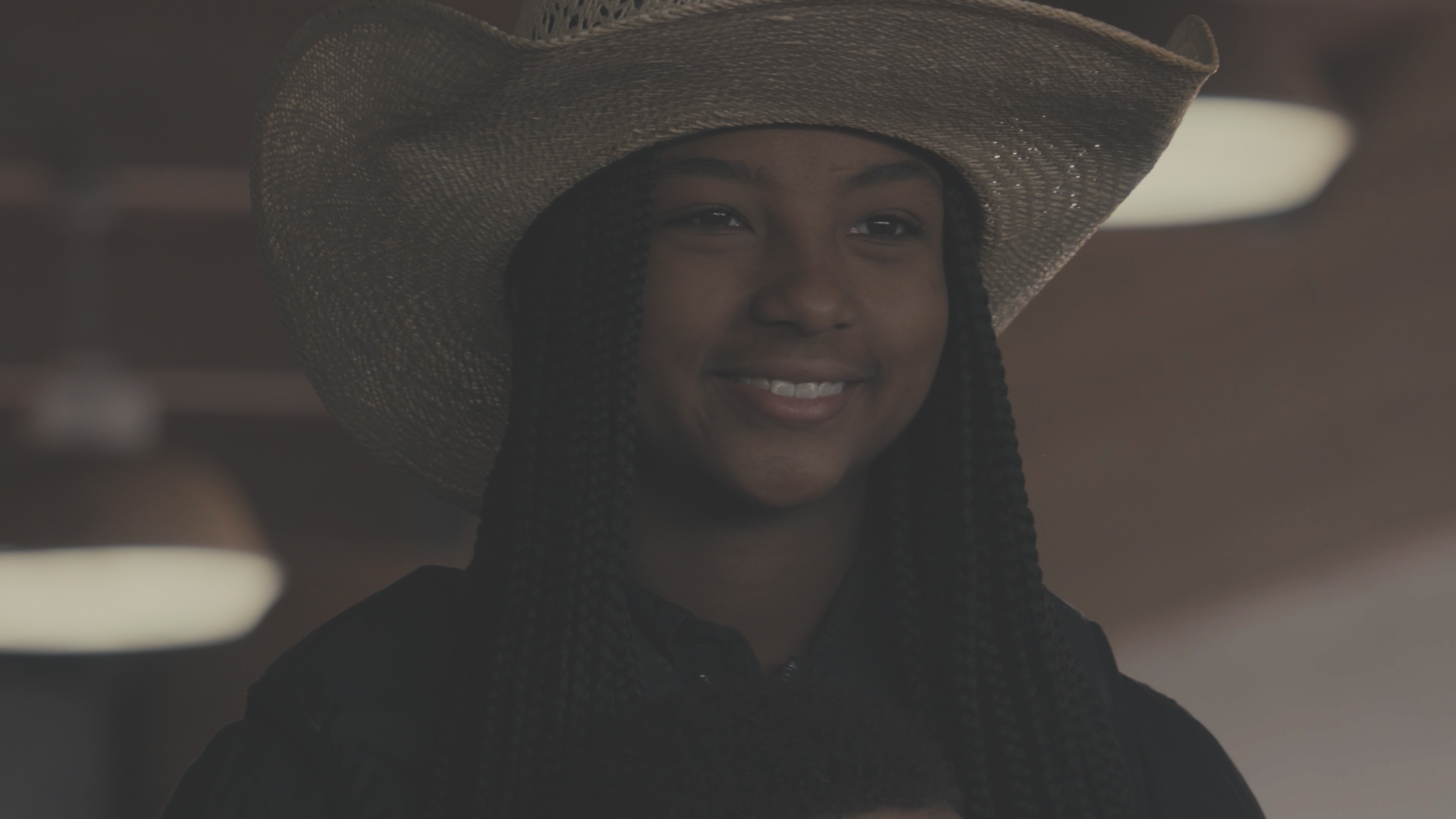 Young woman in straw cowboy hat smiling warmly in a barn