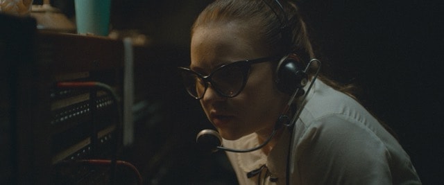 Young woman in cat-eye glasses and headset at a vintage radio switchboard