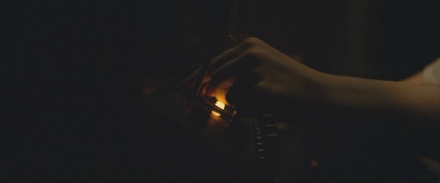 Hands lighting a match in near-total darkness