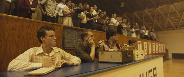 Young men at a press table in a packed gymnasium during a basketball game
