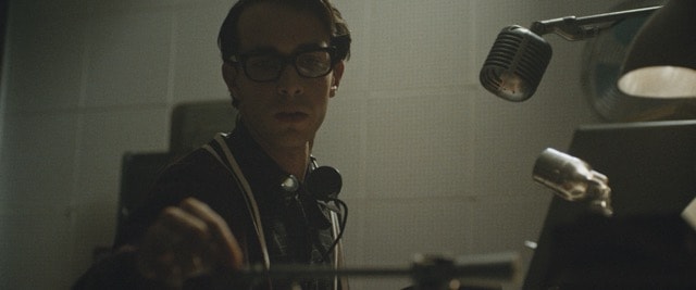 Young man in thick-rimmed glasses at a vintage radio microphone