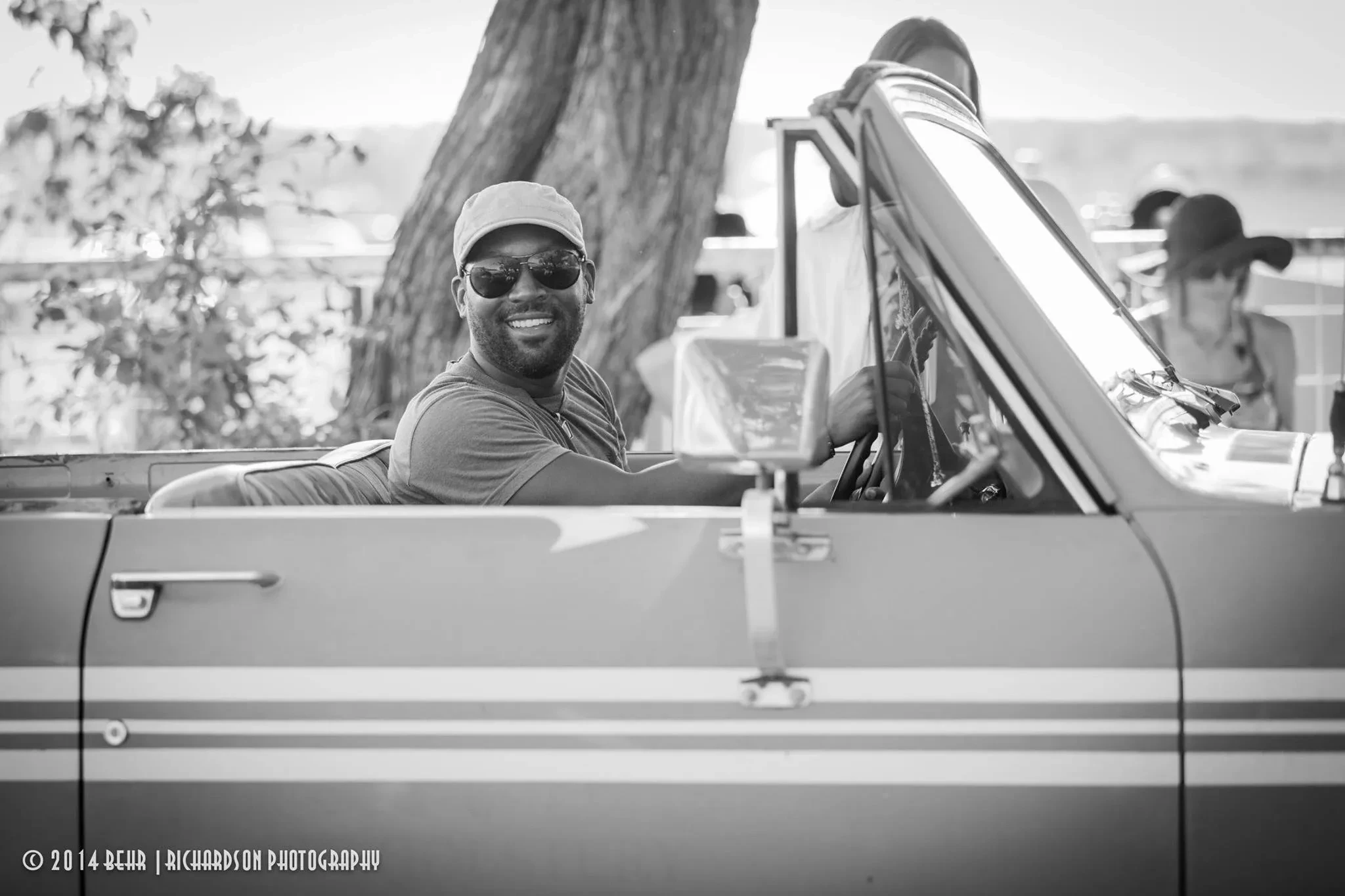 Man smiling in sunglasses behind the wheel of a convertible