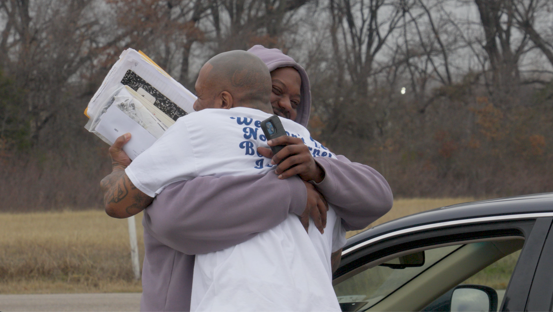 Two people embracing outside a car on a grey winter day