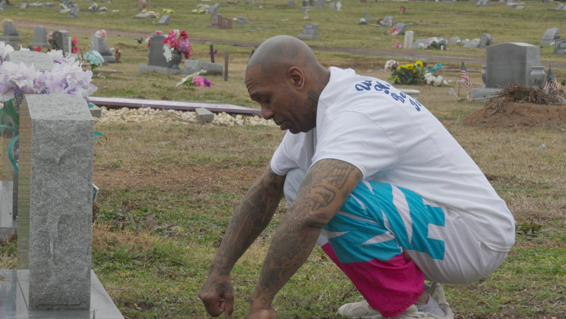 Tattooed man kneeling at gravestone in cemetery